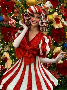 a woman in a red and white dress standing next to a christmas tree with decorations on it