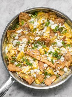 a skillet filled with nachos topped with cheese and cilantro leaves