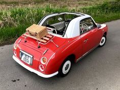 a small red car parked on the side of the road with a box strapped to it's roof