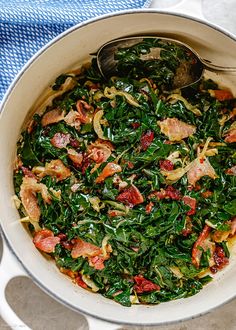 a pot filled with spinach and meat on top of a blue towel next to silver spoons