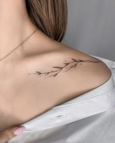 the back of a woman's shoulder with a branch tattoo on it