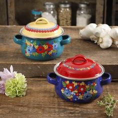 three colorful pots sitting on top of a wooden table next to garlic and other items