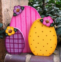 three colorful vases sitting on top of a brick wall next to plants and flowers