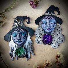 two metal wall hangings with faces and witches on them sitting on a wooden surface