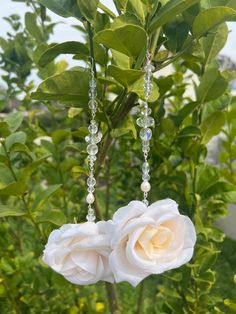 two white roses hanging from a branch with crystal beaded earrings attached to the stems