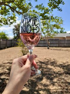 someone holding up a wine glass with the word wine not written on it in front of a tree