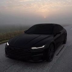 a black car is parked on the side of the road with fog in the background