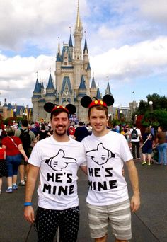 two men standing in front of a castle with mickey mouse ears on their heads and he's mine shirt