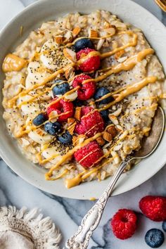 a bowl of oatmeal topped with berries and nuts next to a spoon