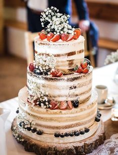 a wedding cake with strawberries and berries on top is sitting on a table in front of the groom