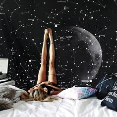 a woman laying on top of a bed in front of a wall with stars and the moon