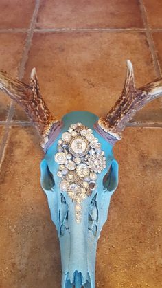 an animal's skull is adorned with jewels and beads on the floor in front of a tile wall