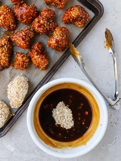 a bowl of sauce next to some meatballs on a baking sheet with spoons