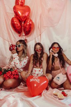 three women sitting on the floor with red balloons and heart - shaped balloons in front of them