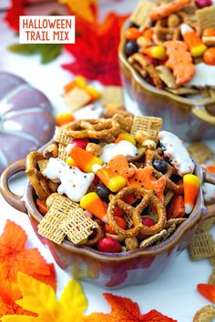 two bowls filled with halloween trail mix on top of a table covered in fall leaves