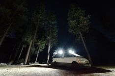 a white van parked in the middle of a forest at night with its lights on