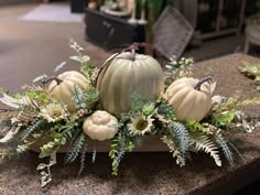 an arrangement of white pumpkins and greenery on a counter