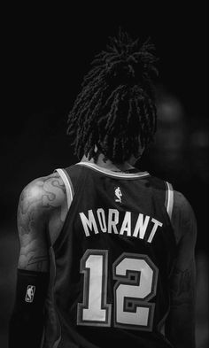 a man with dreadlocks standing in front of a black background wearing a basketball uniform