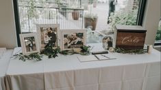 the table is set up with photos and greenery for an elegant wedding reception in front of a large window