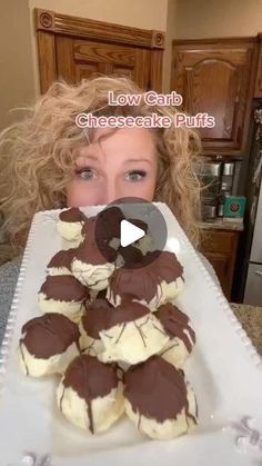 a woman holding up a tray of chocolate covered desserts with the words low carb cheesecake puffs in front of her face