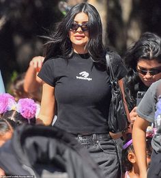 a woman with long black hair and sunglasses walking in front of some other people on the street