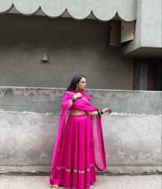 a woman in a pink outfit standing on the sidewalk with her arms crossed and looking off to the side