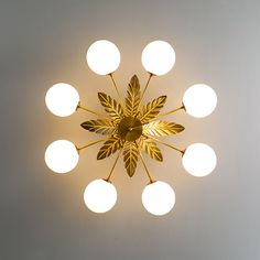 a circular light fixture hanging from the ceiling with white balls around it and a gold leaf design