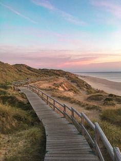 a wooden walkway leading to the beach at sunset with sand dunes in the back ground