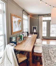 a long wooden table sitting in the middle of a living room next to two windows