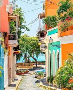 an alley way with colorful buildings and palm trees on either side that leads to the ocean