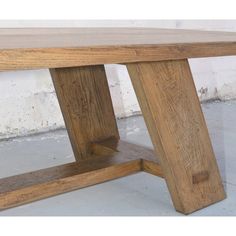 a wooden bench sitting on top of a cement floor next to a white brick wall