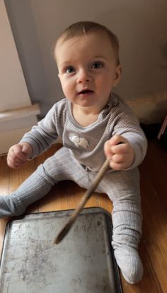 a baby sitting on the floor with a stick in it's hand