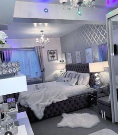 a bedroom decorated in silver and white with chandelier above the bed, mirror on the wall