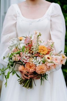 a woman in a white dress holding a bouquet of orange and pink flowers on her wedding day