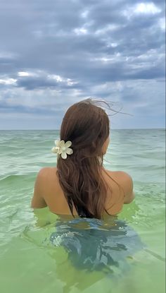 a woman is sitting in the water with her back to the camera and looking out at the ocean