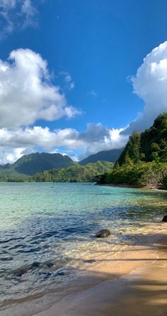 the beach is clear and blue with white clouds in the sky above it, as well as some green trees