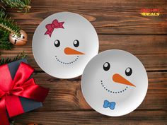 two white plates with snowmen painted on them next to christmas decorations and a red bow