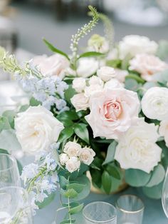 a vase filled with white and pink flowers on top of a table next to wine glasses