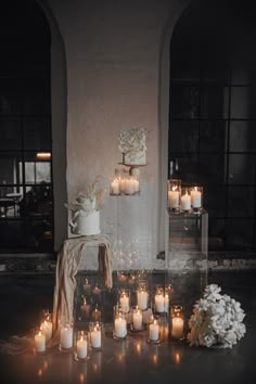 candles are arranged on the floor in front of a wall with flowers and vases