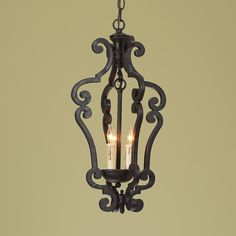 an iron hanging light with two candles in the center and one candle lit inside it