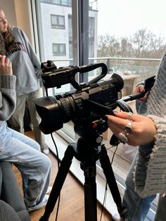 a camera set up on a tripod in front of a window with people standing around