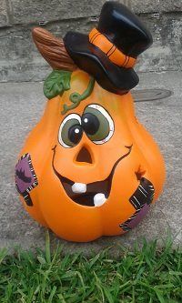 a ceramic pumpkin with a hat on it's head sitting in the grass next to a stone wall