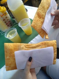 the person is holding two pieces of bread with napkins on them and some drinks in front of them