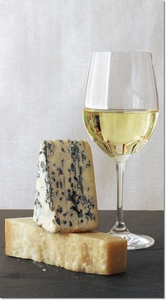 a piece of cheese next to a glass of wine