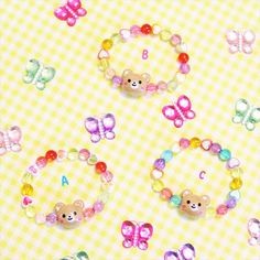 the bear and butterfly bracelets are made from plastic beads, which have been placed on a checkered tablecloth