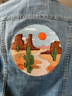 a person wearing a jean jacket with an embroidered desert scene on it's back