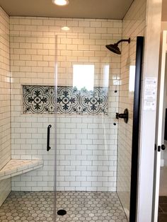 a walk in shower sitting next to a white tiled wall and floor with black accents