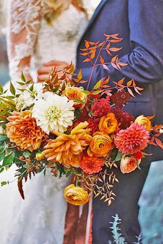 a bride and groom standing next to each other in front of an orange flower bouquet