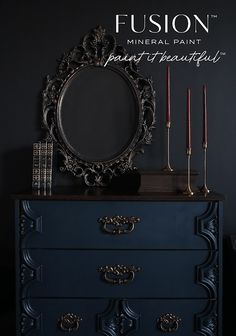 a black dresser with candles and a mirror on it's top, in front of a dark wall