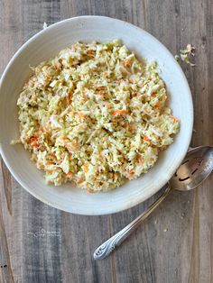 a white bowl filled with coleslaw and carrots next to a silver spoon